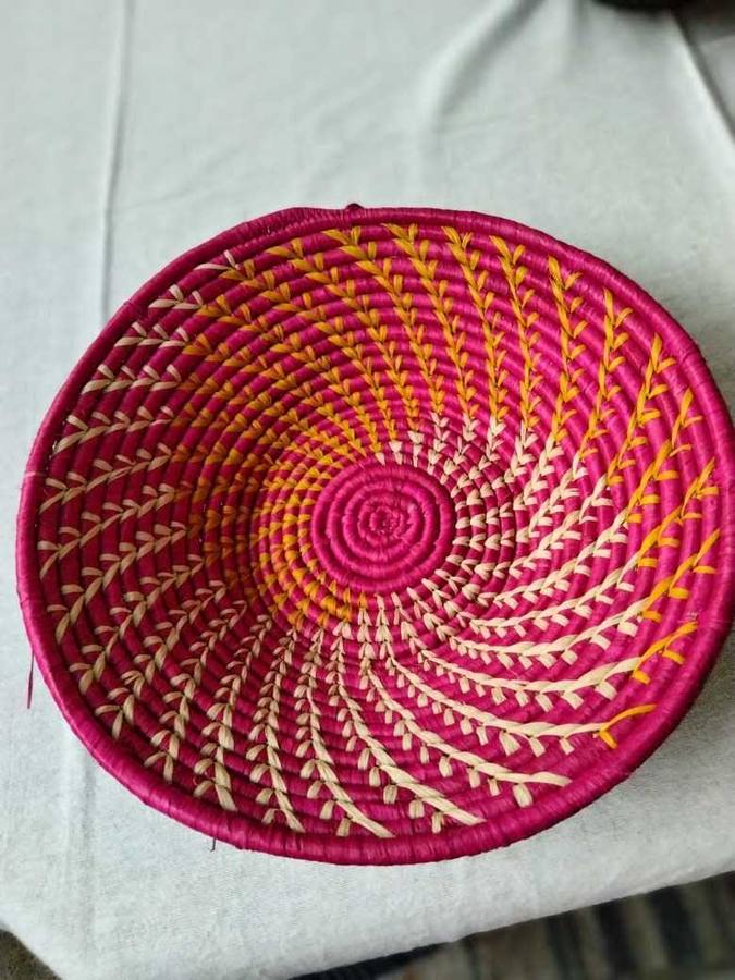 Magenta and marigold woven raffia bowl with spiraling pattern