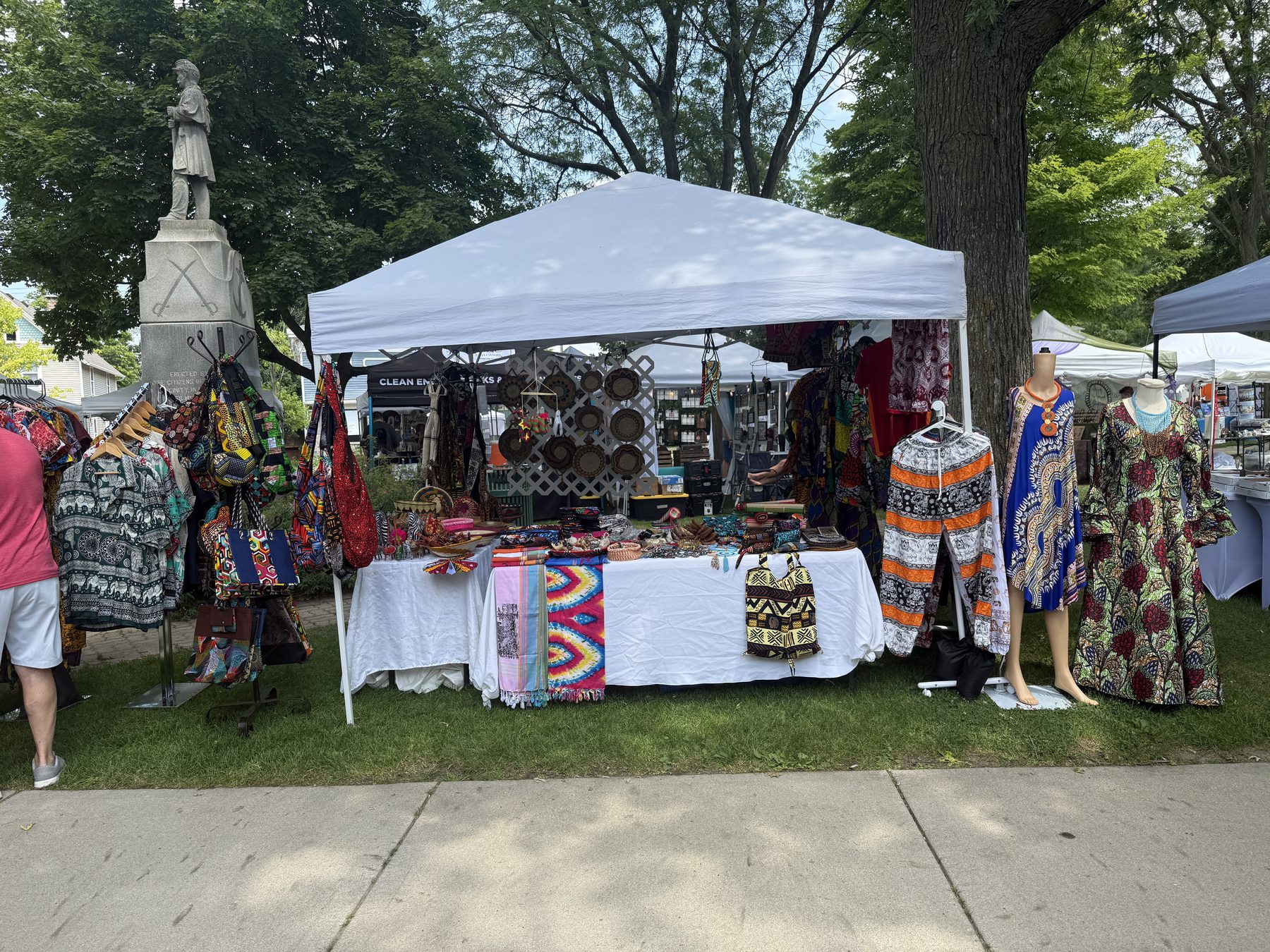 Imani Handmade Crafts pop-up tent set up at an outdoor market, with dresses, bags, and baskets on display