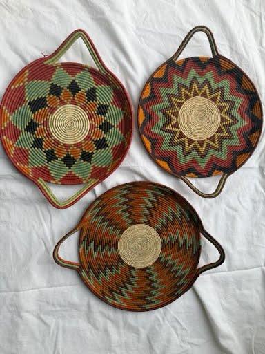 Three round woven trays with handles, in red, orange, and rust star and chevron patterns
